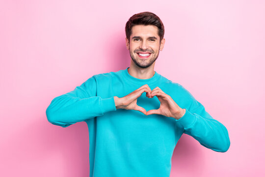 Photo portrait of attractive young man arms showing heart figure shape romantic dressed stylish blue look isolated on pink color background