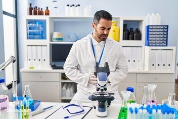 Young hispanic man with beard working at scientist laboratory with hand on stomach because indigestion, painful illness feeling unwell. ache concept.