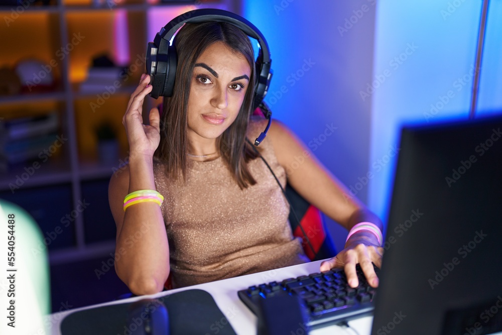 Poster Young beautiful hispanic woman streamer playing video game using computer at gaming room