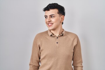 Fototapeta premium Non binary person standing over isolated background looking away to side with smile on face, natural expression. laughing confident.