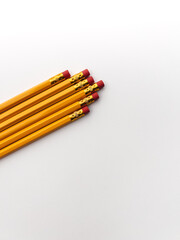 Stationery on office table. Isolated yellow pencils with red rubbered tip on the white background in a row 