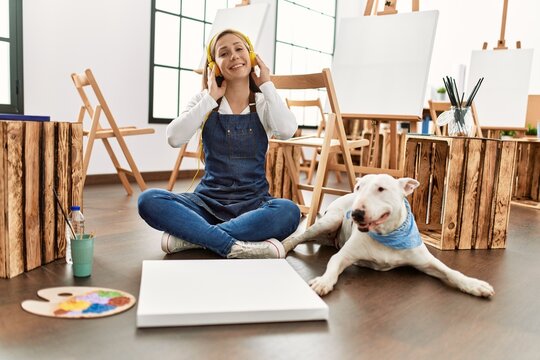 Young caucasian woman listening to music with dog at art studio