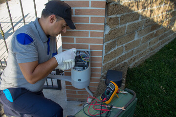 Electrician wiring and repairing the motor of an automatic gate in a driveway.
