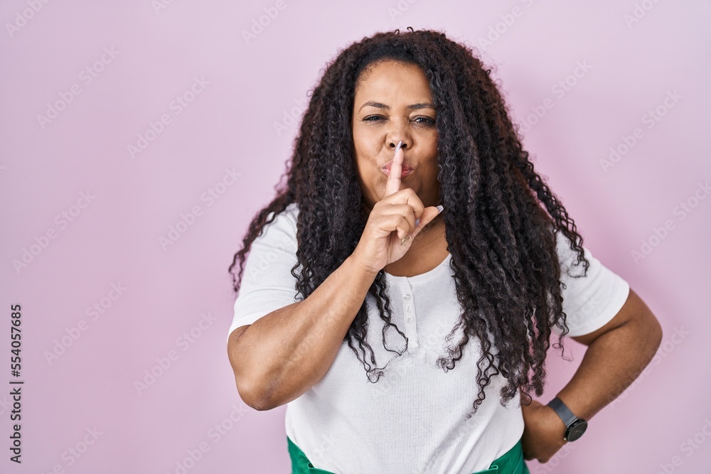 Sticker Plus size hispanic woman standing over pink background asking to be quiet with finger on lips. silence and secret concept.