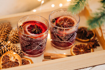 Cozy close-up of two glasswes with mulled wine. Christmas drink. Xmas tree and garland lights. Winter beverage