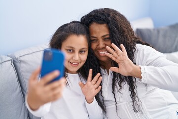 Mother and daughter having video call sitting on sofa at home