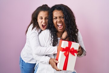 Mother and young daughter holding with presents angry and mad screaming frustrated and furious, shouting with anger. rage and aggressive concept.