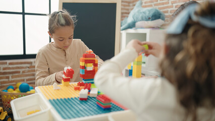 Adorable toddler playing with construction blocks sitting on table at classroom