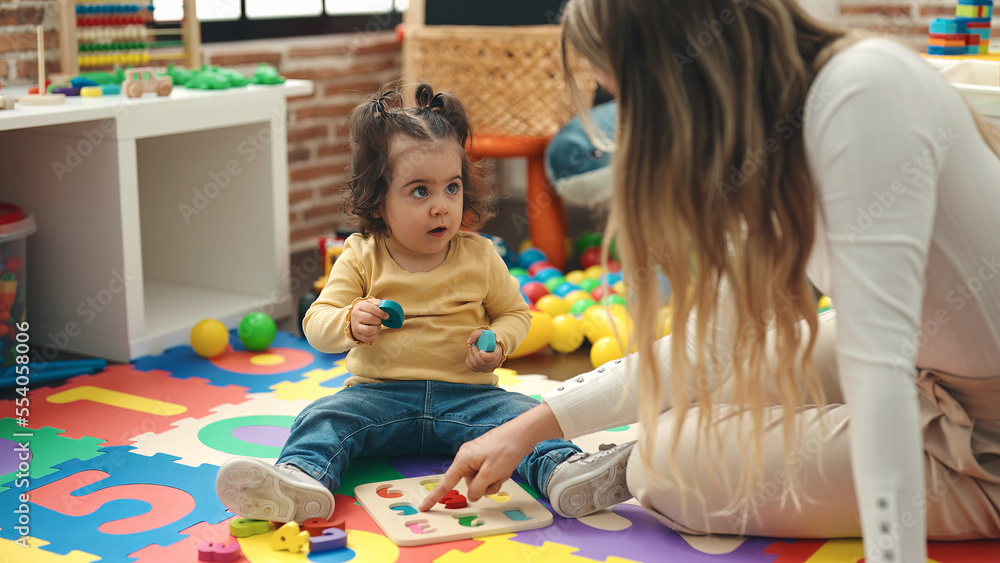 Poster adorable hispanic girl playing with maths puzzle game sitting on floor at kindergarten