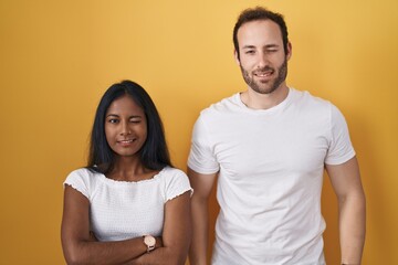 Interracial couple standing over yellow background winking looking at the camera with sexy...