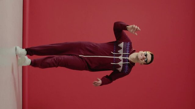 A young man in sunglasses and a Christmas kigurumi dances on a red background.