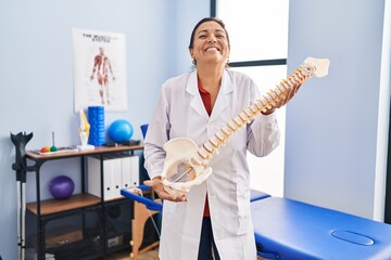 Middle age hispanic woman holding anatomical model of spinal column smiling and laughing hard out...