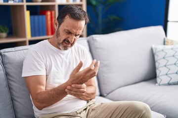 Fototapeta premium Middle age man sitting on sofa suffering for wrist pain at home