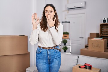 Young hispanic woman holding keys of new home covering mouth with hand, shocked and afraid for mistake. surprised expression