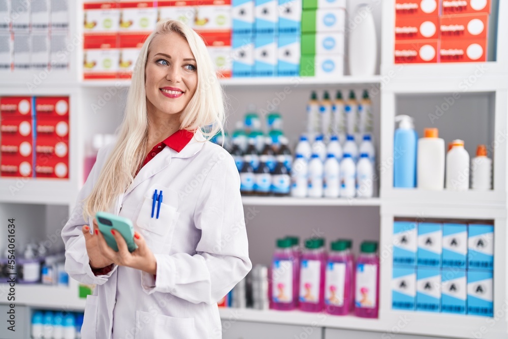 Sticker Young blonde woman pharmacist using smartphone working at pharmacy