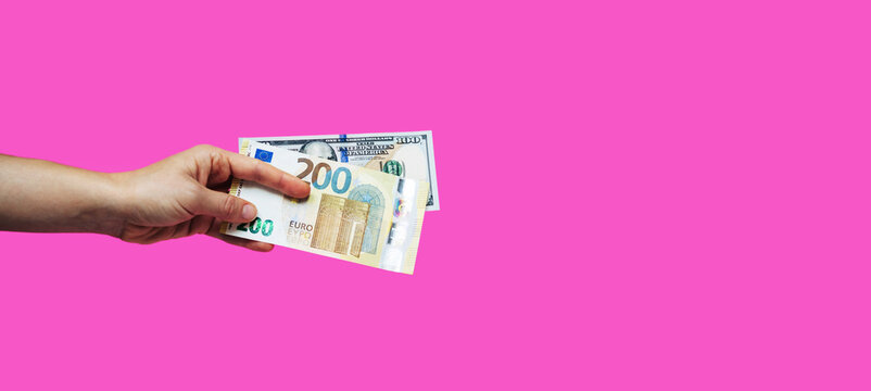 Money 200 euro bill and 100 american dollars bill in hand against pink background.