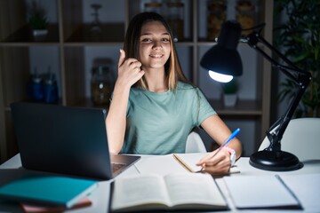 Teenager girl doing homework at home late at night doing happy thumbs up gesture with hand. approving expression looking at the camera showing success.