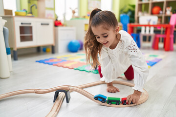 Adorable hispanic girl playing with cars toy sitting on floor at kindergarten