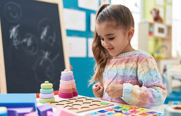 Adorable hispanic girl playing with maths puzzle game standing at kindergarten - obrazy, fototapety, plakaty