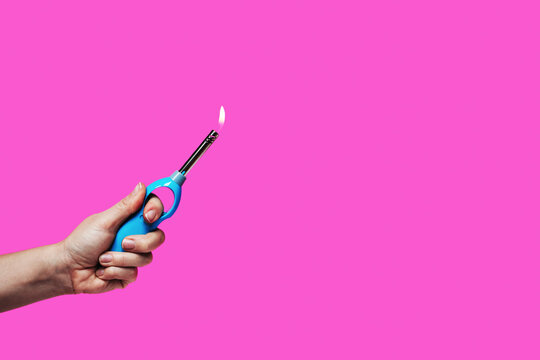 Ignitor lighter for gas stove and burner in hand against pink background.