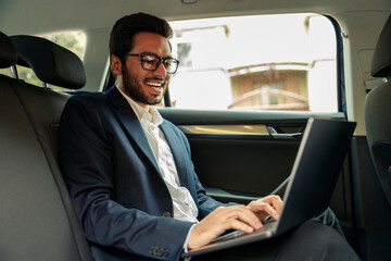 Fototapeta na wymiar Attractive businessman in suit working laptop while riding in car to office