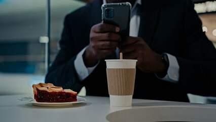 Fototapeta na wymiar Unrecognizable man African businessman entrepreneur with mobile phone browsing chatting make picture photo blogger vlogger male at table with smartphone in cafe with cake coffee messaging in cafeteria