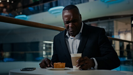 African American middle-aged businessman entrepreneur cafe visitor man sitting eating in cafeteria dissatisfied with bad cake disgust pie dessert trouble drink nasty tea tasteless coffee unpleasant - obrazy, fototapety, plakaty