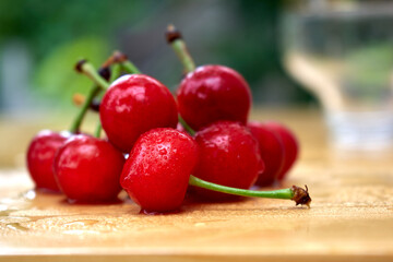 A group of red cherries with water drops lying on a wooden table