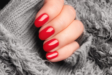 Female hand with beautiful manicure - red nails on gray fluffy knitted fabric. Nail care concept