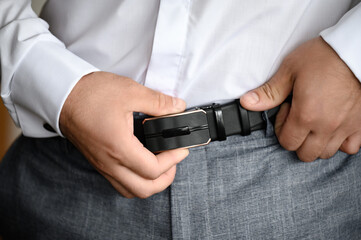 A man puts on a belt on his pants, a classic of a businessman's man.