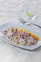 Ceviche, typical fish-based dish of Peruvian cuisine, presented in a rectangular plate on a table with white tablecloth.