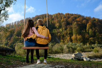 a couple of school children ride on a big swing in the park near the river.