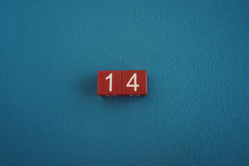 Wooden Viva Magenta cubes with number 14 on blue background close-up top view. Concept of date or...