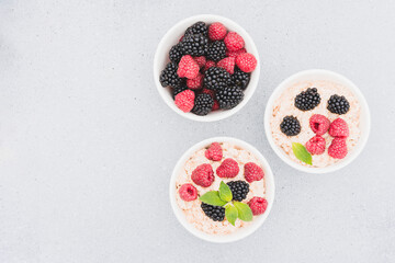 Oatmeal porridge garnished with various berries in white bowls on concrete table background with copy space. Morning superfood porridge recipe