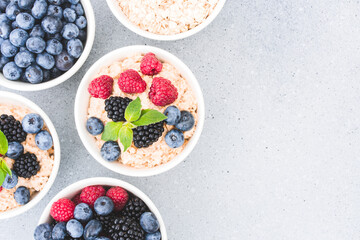 Healthy breakfast - bowls with oatmeal porridge garnished with various berries on concrete table background with copy space. Morning superfood porridge recipe