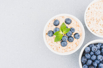 White bowls with oatmeal porridge and organic fresh blueberry on light gray concrete table background with copy space. Morning superfood porridge recipe. Healthy breakfast ideas