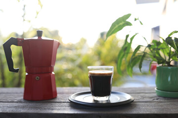 Red moka pot and coffee glass cup on wooden table with plant pot
