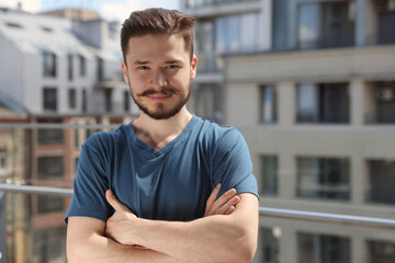 Handsome man crossing his arms on balcony in city. Space for text