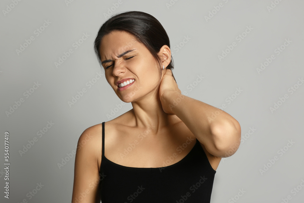 Canvas Prints Young woman suffering from neck pain on grey background