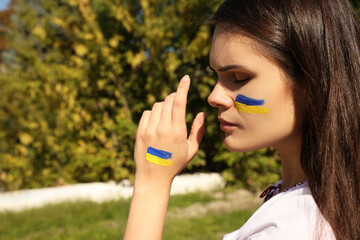 Young woman with drawings of Ukrainian flag outdoors, closeup. Space for text