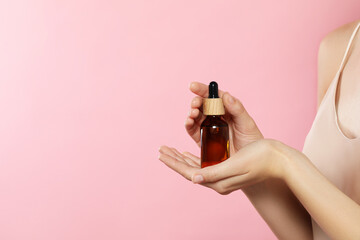 Young woman with bottle of essential oil on pink background, closeup. Space for text