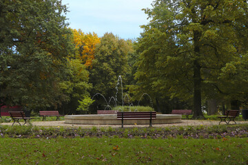Beautiful view of public city park with benches near fountain on autumn day