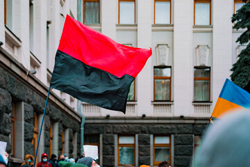 Red and black black banner of Ukrainian Insurgent Army and Ukrainian blue and yellow flag waves near a building during strike. UPA. Battle. Protest. Revolution. Nationalist movement. Riot. Street - obrazy, fototapety, plakaty
