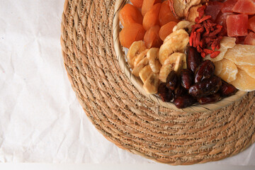 Wicker basket with different dried fruit on paper, top view. Space for text