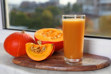 Tasty pumpkin juice in glass, whole and cut pumpkins on windowsill indoors