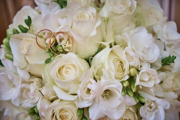 The bride's bouquet consists of white roses and pink hydrangeas, wedding rings on the bouquet. Close-up.