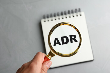 Alternative dispute resolution. Closeup of woman holding magnifier glass over abbreviation ADR in...