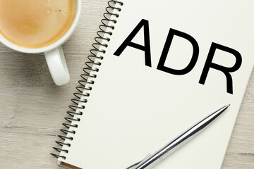 Alternative dispute resolution. Notebook with abbreviation ADR, pen and cup of coffee on wooden...