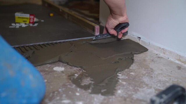 Flooring and tiling. Professional tiler placing floor tiles on adhesive surface.