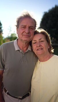 A happy married older couple looking at camera at park with during sunny day backlight. Close up of senior faces of 70s husband and wife in Vertical Video